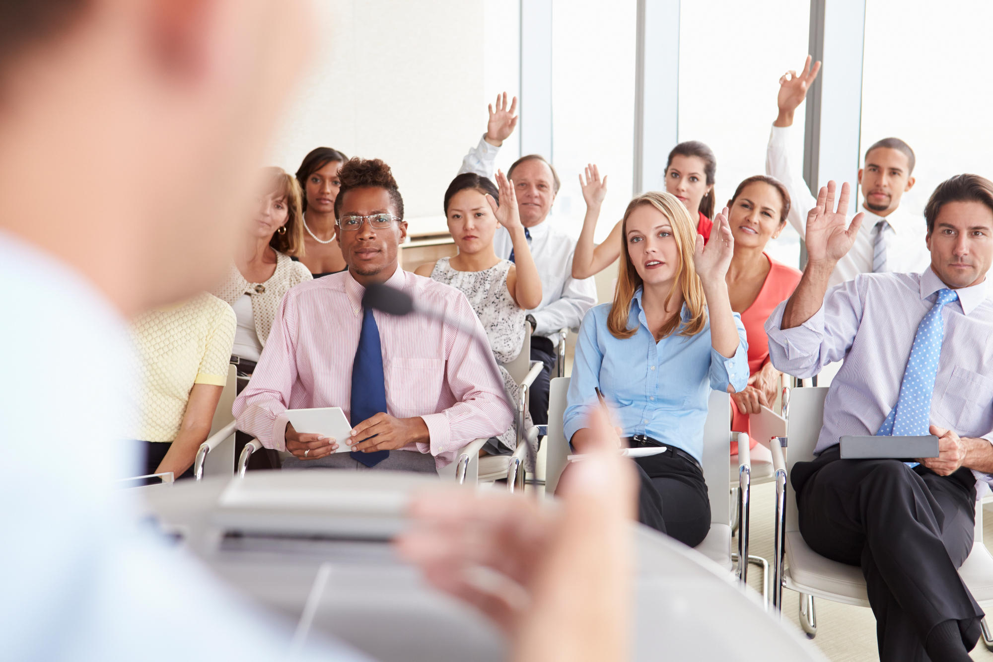 A group of people reasing their hands to ask someone giving a presnetation a question