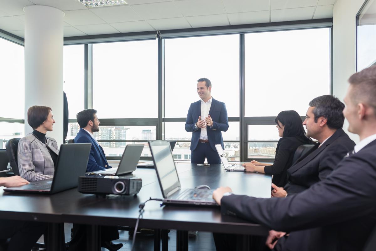 A group of business professionals engaged in discussion around a conference table in a meeting room.